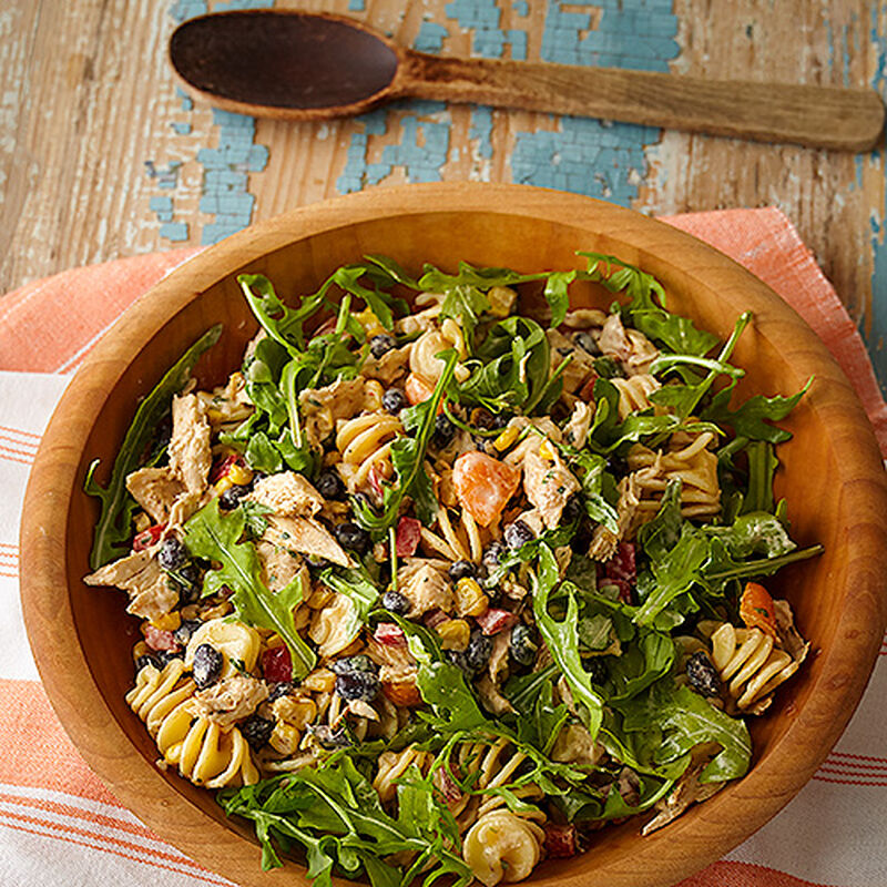 A bowl of pasta salad with bell peppers, arugula, tomatoes and avocado.