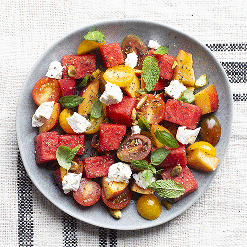 A bowl of salad consisting of watermelon, feta cheese, mint, nectarines and cherry tomatoes. 